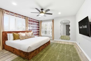 Un dormitorio con cama, ventilador de techo, televisor y vista al exterior.