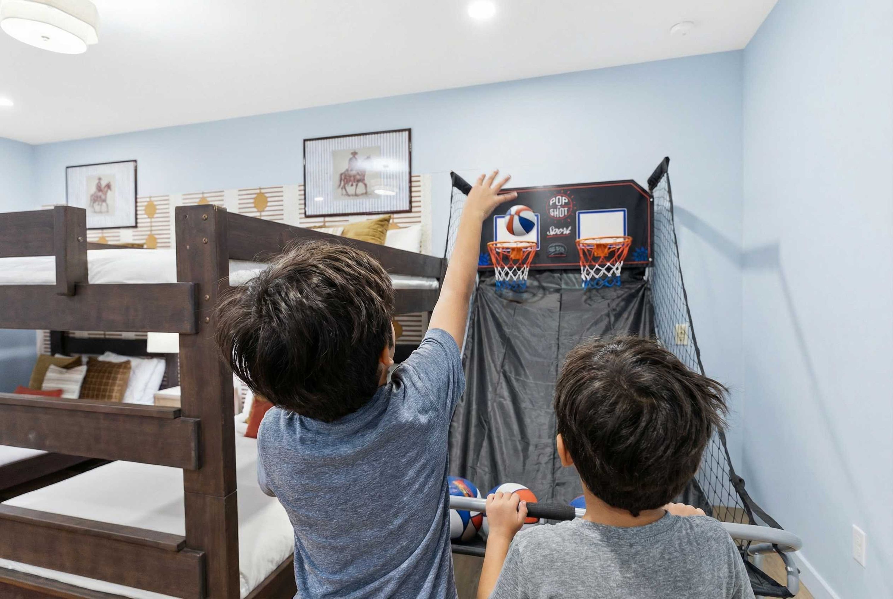 Una cama litera con dos niños jugando baloncesto en una habitación de paredes azul claro y cuadros en la pared.