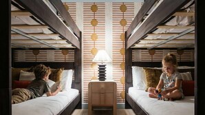 A room with bunk beds, a central table with a lamp, and a patterned wall. - Ultimate Backyard Pool Game Room Kid s Room (San Antonio)
