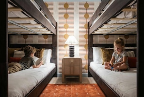 A room with bunk beds, a central table with a lamp, and a patterned wall. - Ultimate Backyard Pool Game Room Kid s Room (San Antonio)