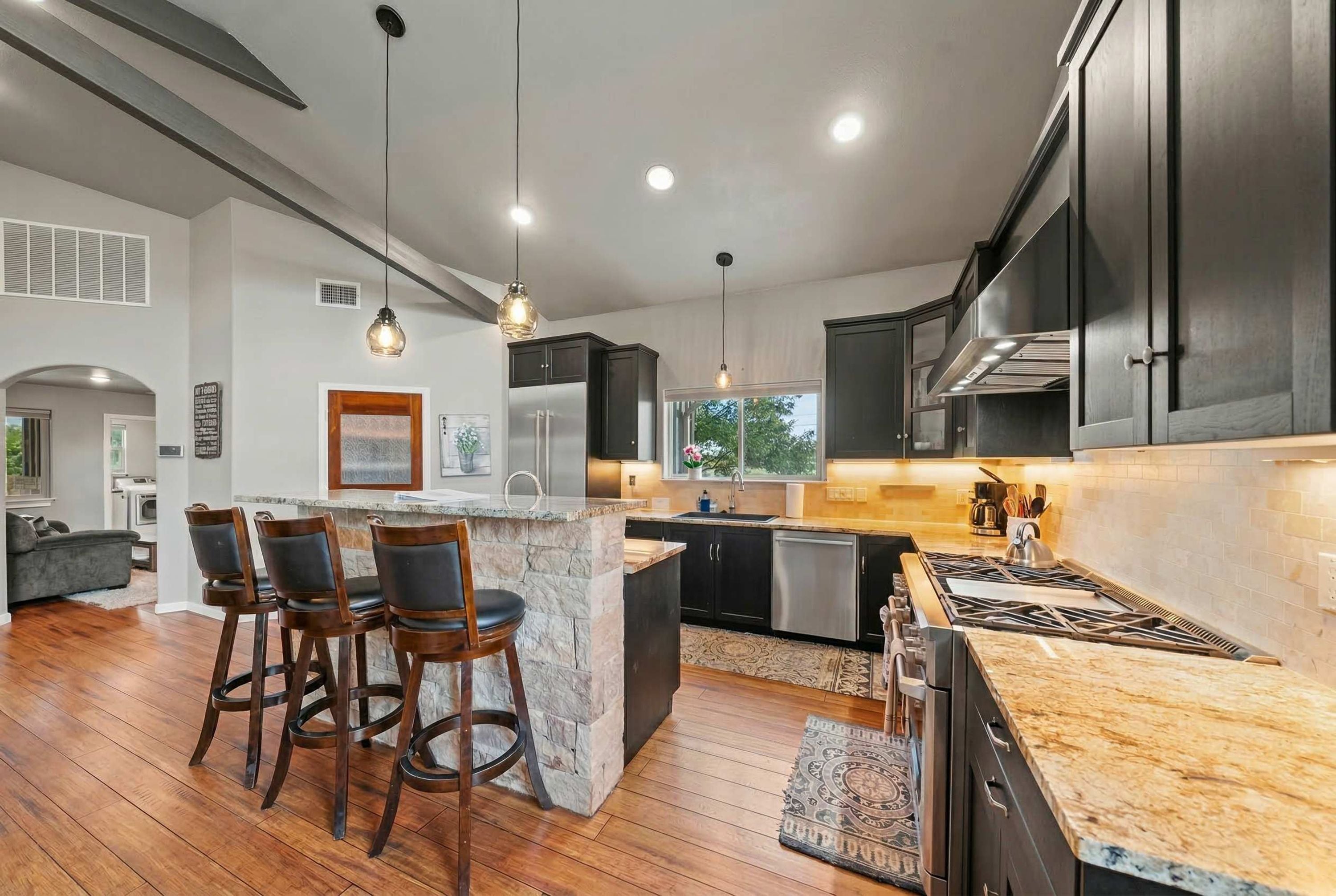 A modern kitchen with a central island, bar stools, stainless steel appliances, and a view to the outdoors.