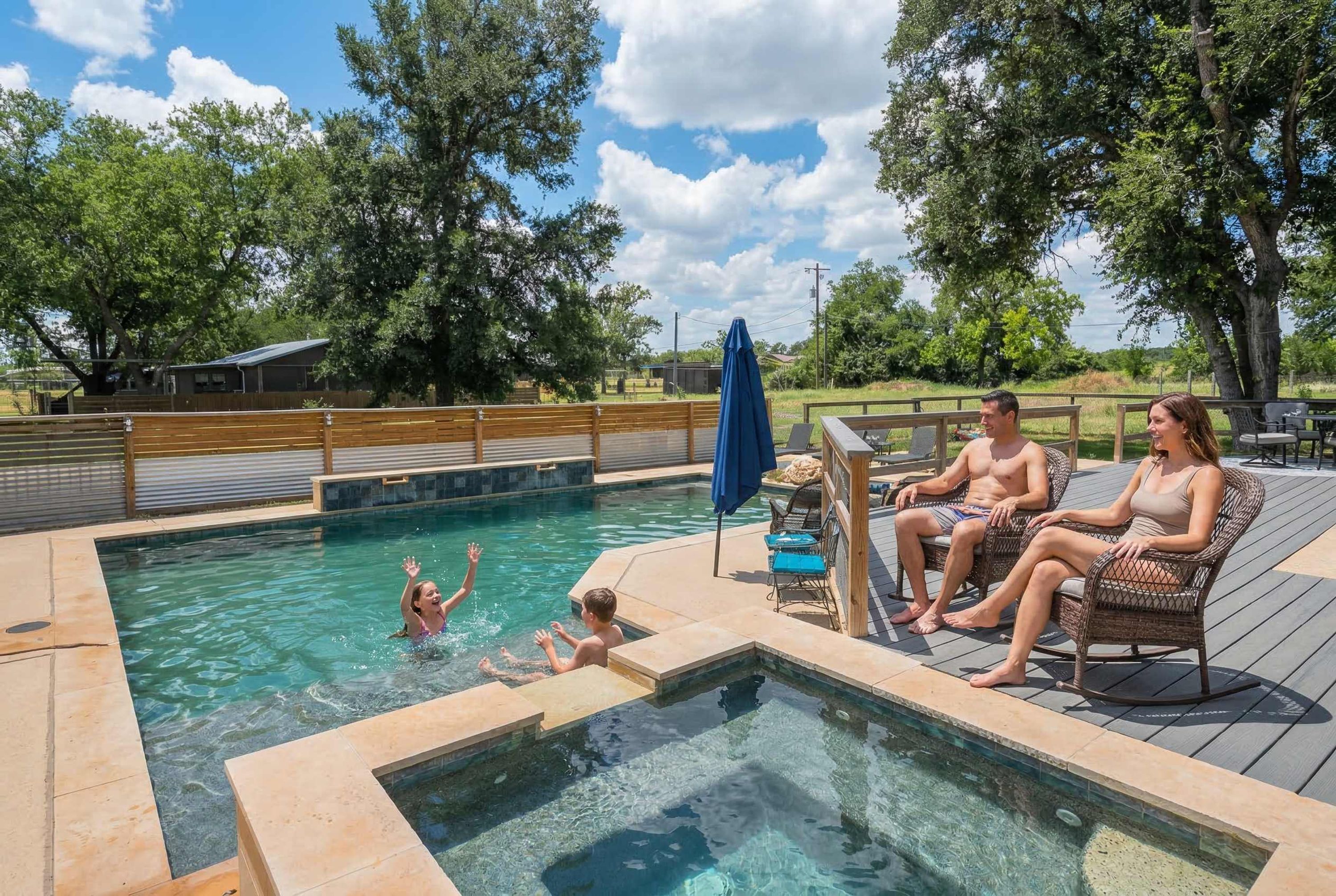 A swimming pool area with a wooden deck, lounge chairs, and a hot tub.