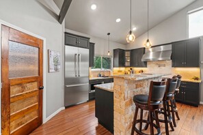 A modern kitchen with a stone island, stainless steel appliances, and dark cabinetry. - 2 Home Getaway-pool-hot Tub-pickleball Court (Fredericksburg)