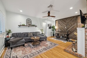 A modern living room with a grey sofa, a wooden coffee table, and a patterned rug. - The Glow-up House Pool Spa Glam Room (Phoenix)