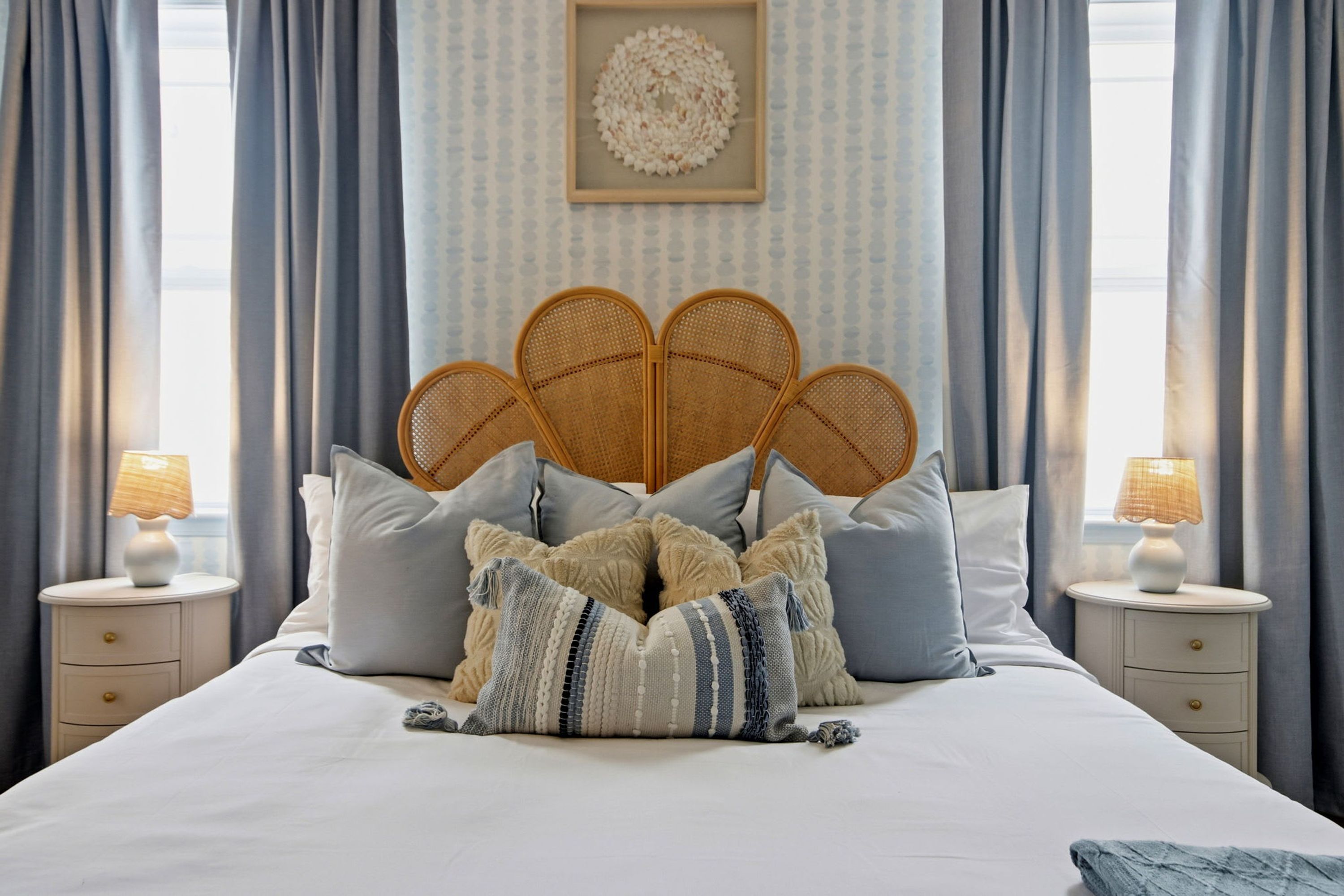 A bed with a unique headboard, multiple pillows, bedside tables with lamps, and a patterned wall.