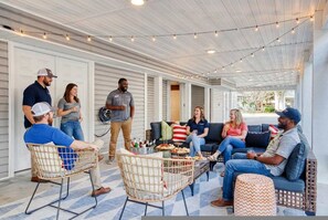 A covered outdoor seating area with string lights, wicker chairs, a coffee table with snacks, and a sofa. - Golf Sim Theater Games Walk to Beach Sleeps 28 (North Myrtle Beach)