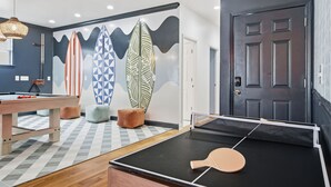 Una habitació amb taula de ping-pong, taula de bitlles i un mur amb dissenys de taules de surf.