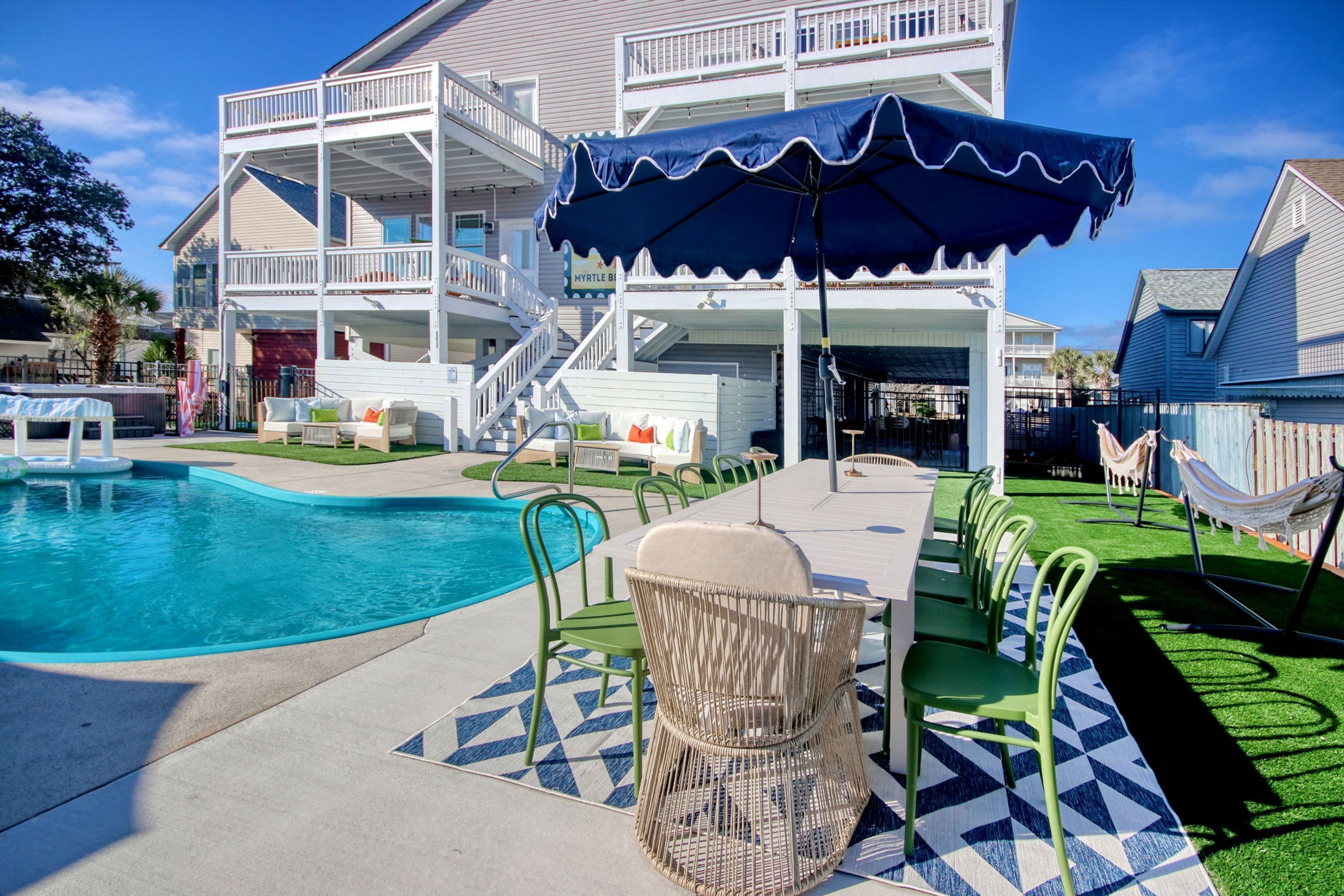 A pool area with a covered seating area, a dining table with chairs, and a hammock.