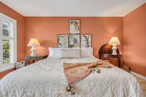 A bedroom with a large bed, two bedside tables with lamps, a window with blinds, and three framed botanical prints on the wall. - Sleeps 24 Waterfront Dock Golf Cart Walk to Beach (Pawleys Island)