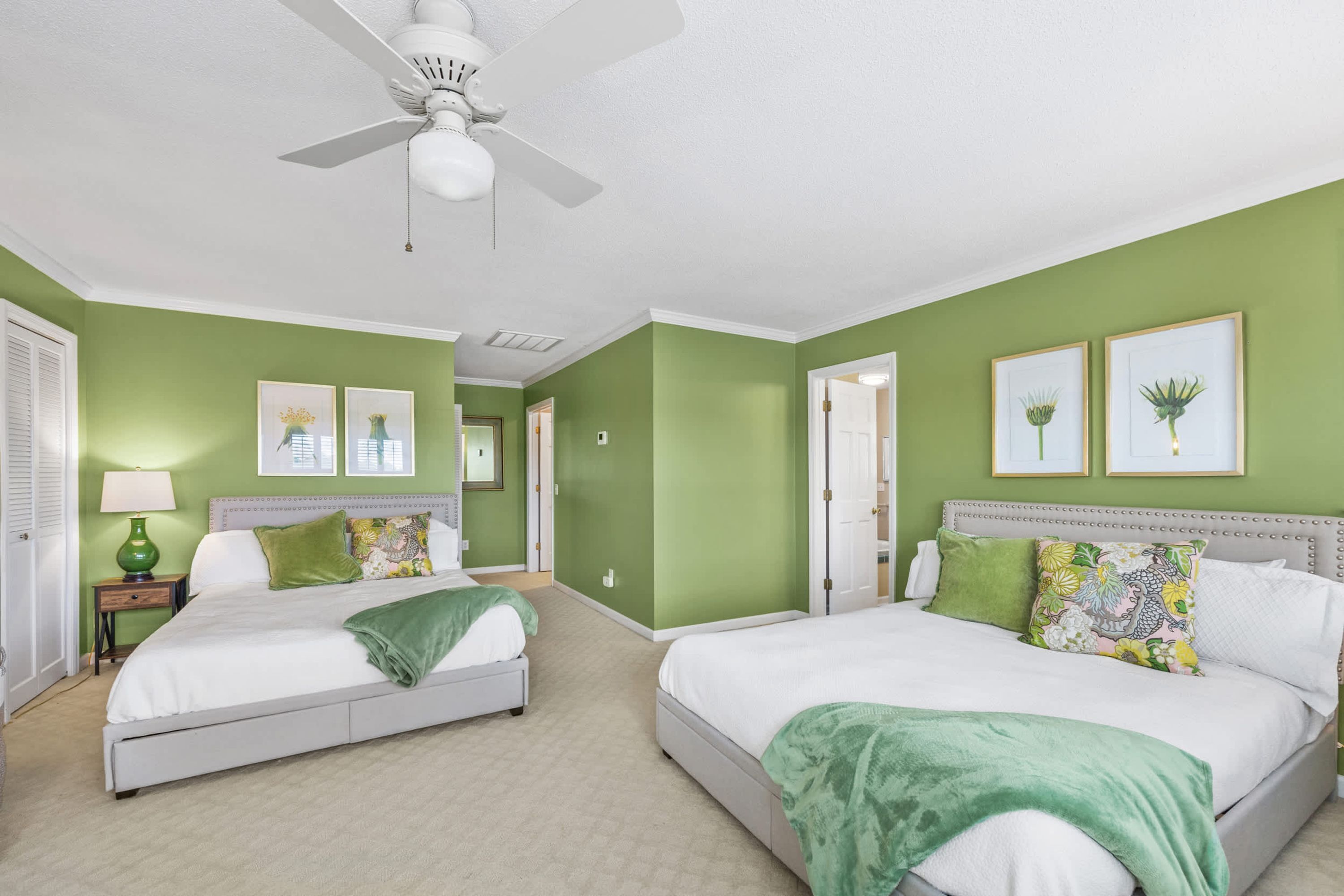 A bedroom with two beds, green walls, and artwork.