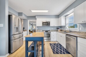 A modern kitchen with stainless steel appliances, white cabinetry, and a wooden table. - Sleeps 24 Waterfront Dock Golf Cart Walk to Beach (Pawleys Island)