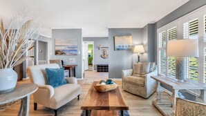Una sala de estar moderna con un sofá color beige, una mesa de centro de madera y un sillón estampado.