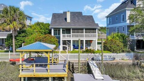 Una propiedad frente al agua con un muelle, un área de estar techada y un edificio de dos pisos con balcón.