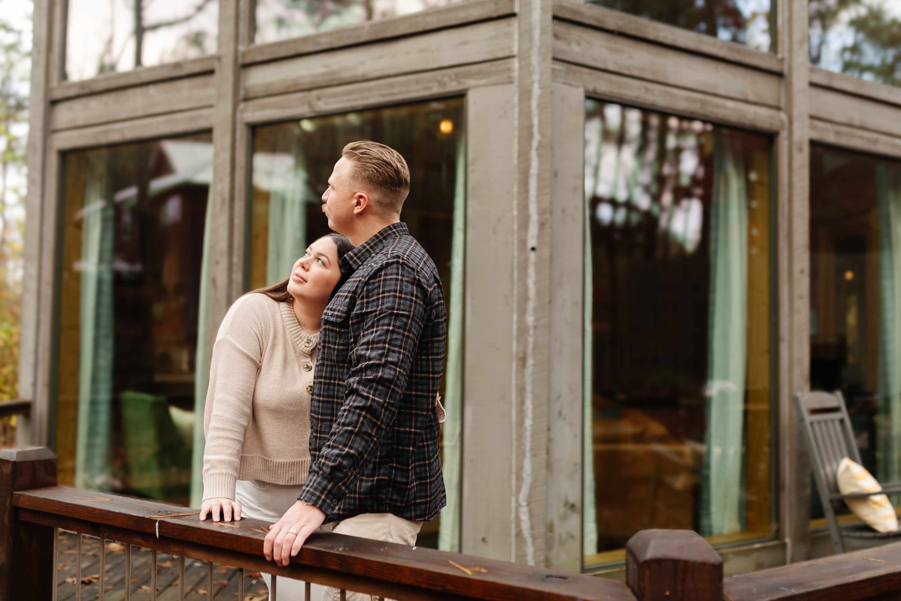 Una pareja está de pie en un balcón con vistas a un edificio de grandes ventanales.