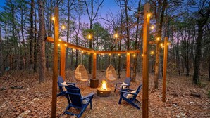 An outdoor seating area with chairs and a fire pit surrounded by a wooden pergola with string lights. - Retro Retreat Stargazing Dome Sauna Hot Tub (Broken Bow)