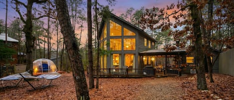 Une cabane moderne dotée de grandes fenêtres, d’un espace de détente extérieur couvert et d’une structure ressemblant à une tente.