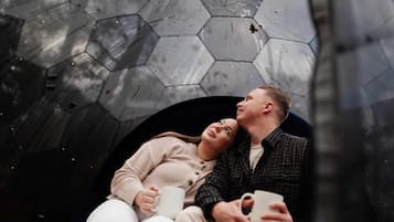 Una pareja sentada en un banco con un muro hexagonal de patrones detrás.