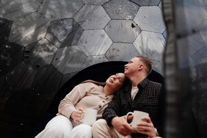 Una pareja sentada en un banco con un muro hexagonal de patrones detrás.