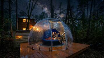 Una tienda en forma de cúpula con techo transparente, un área de estar circular y una terraza de madera.