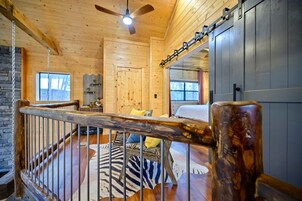 A wooden cabin interior with a balcony, a ceiling fan, and a bed with a zebra-patterned rug.