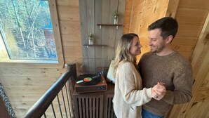 A wooden interior with a record player on a table, a window with a view of trees, and a wooden picket fence. - Retro Retreat Stargazing Dome Sauna Hot Tub (Broken Bow)