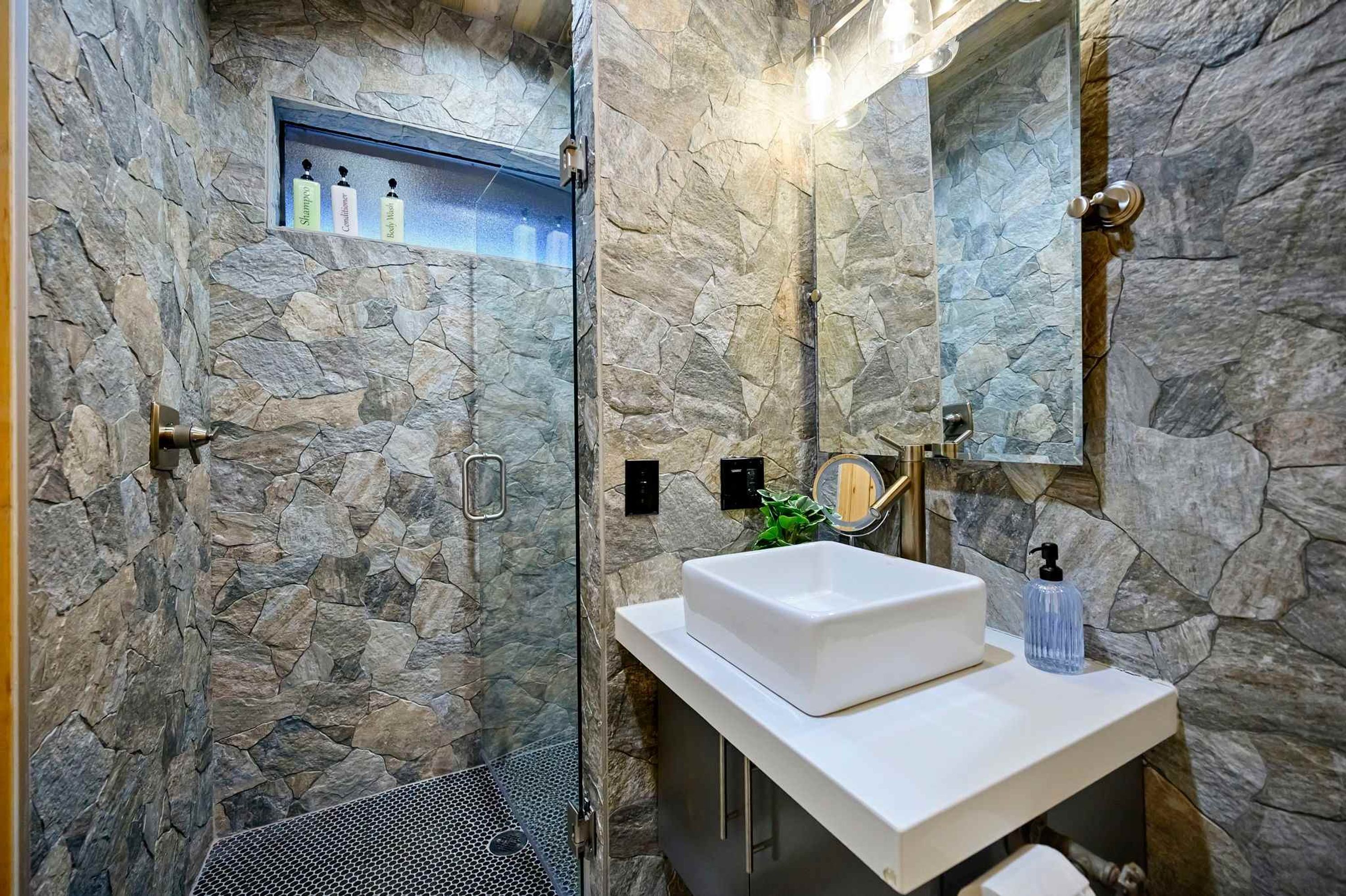 A bathroom with a stone wall, a white sink, a mirror, and a shower area.