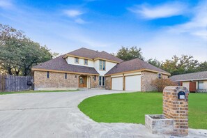 A two-story house with a garage, a driveway, and a well-maintained lawn. - Gathering House Movie Game Room Hot Tub Pool (San Antonio)