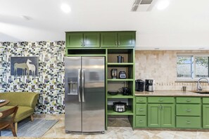 A kitchen with green cabinets, a stainless steel refrigerator, a coffee maker, and a bowl. - Gathering House Movie Game Room Hot Tub Pool (San Antonio)