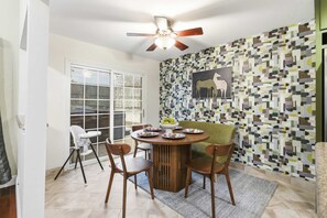 A dining area with a round table, chairs, a ceiling fan, and a patterned wall. - Gathering House Movie Game Room Hot Tub Pool (San Antonio)