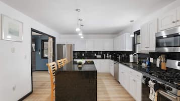 A modern kitchen with white cabinets, a black countertop, stainless steel appliances, and a dining area with a wooden table and chairs.