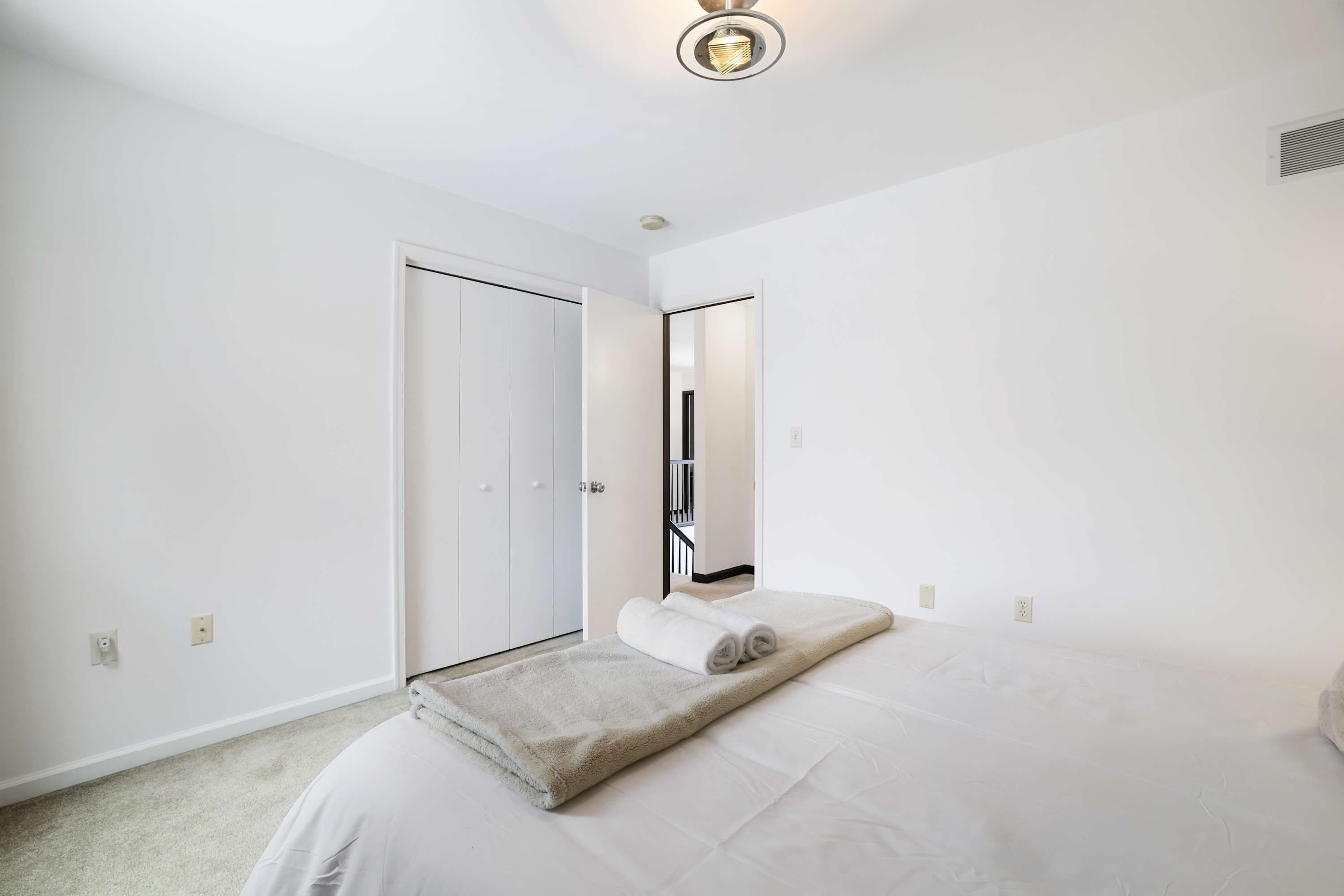 A bedroom with a bed, a white door, a mirror, and a ceiling light fixture.