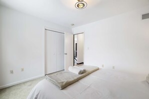 Ein Schlafzimmer mit einem Bett, einer weißen Tür, einem Spiegel und einer Deckenleuchte.