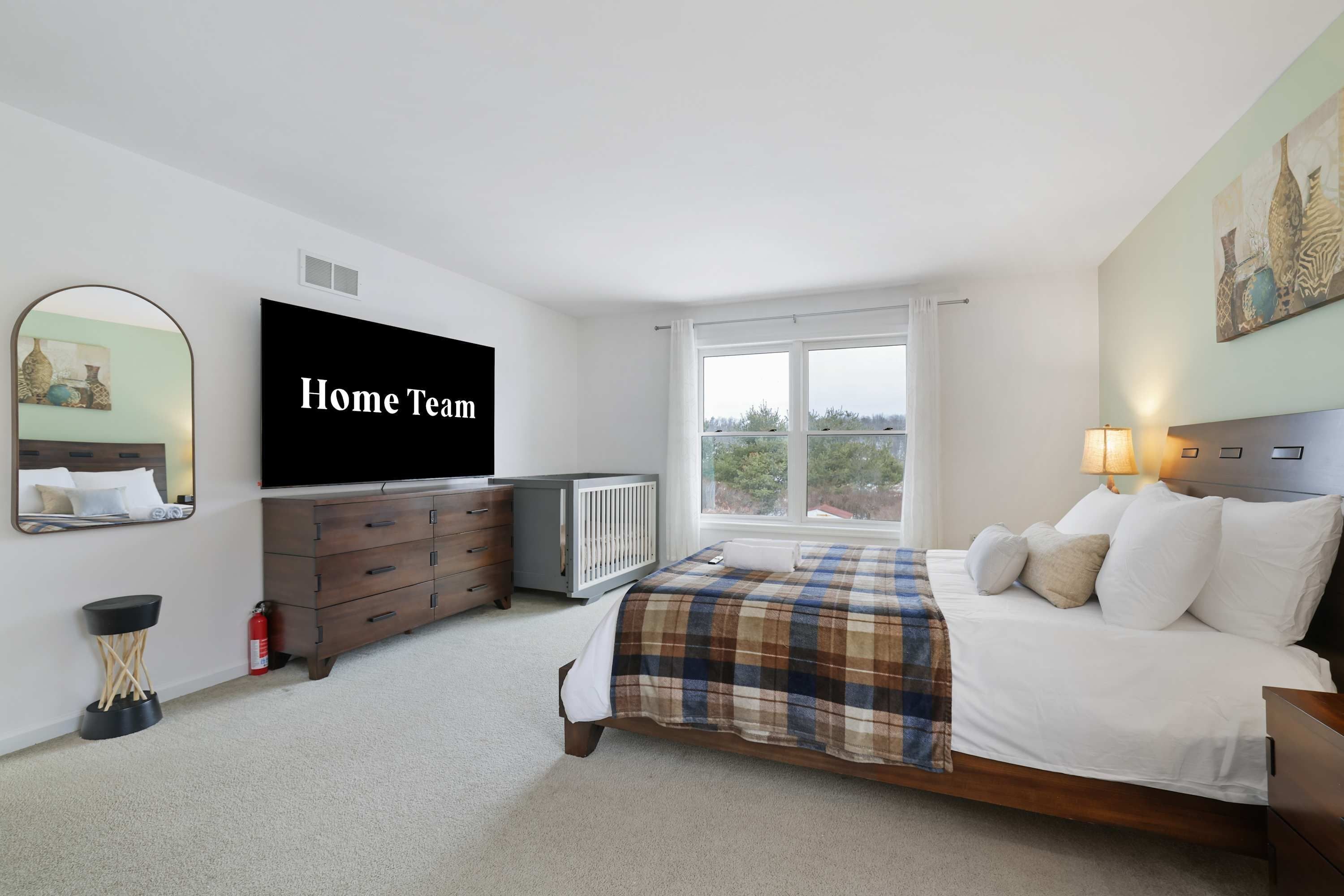 A bedroom with a bed, a dresser, a television, a window, and a painting on the wall.