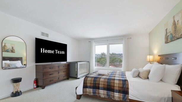 Ein Schlafzimmer mit einem Bett, einem Schminktisch, einem Fernseher, einem Fenster und einem Bild an der Wand.