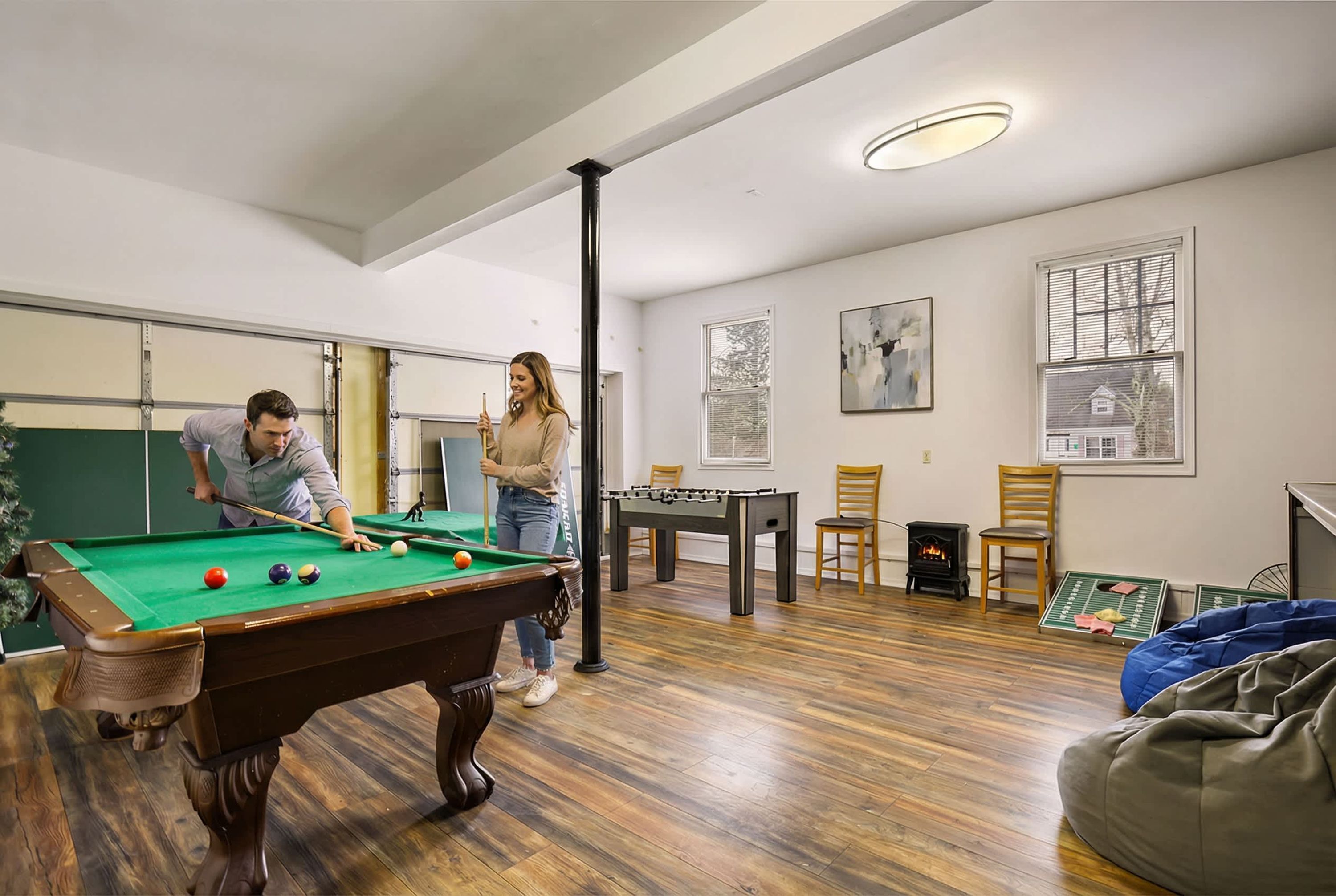 A room with a pool table, a foosball table, and a fireplace.