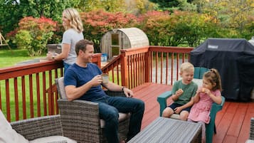 A family on a wooden deck with a grill and a small shed in the background.
