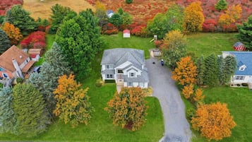 A residential area with a two-story house, a driveway, and surrounding trees with autumn foliage.