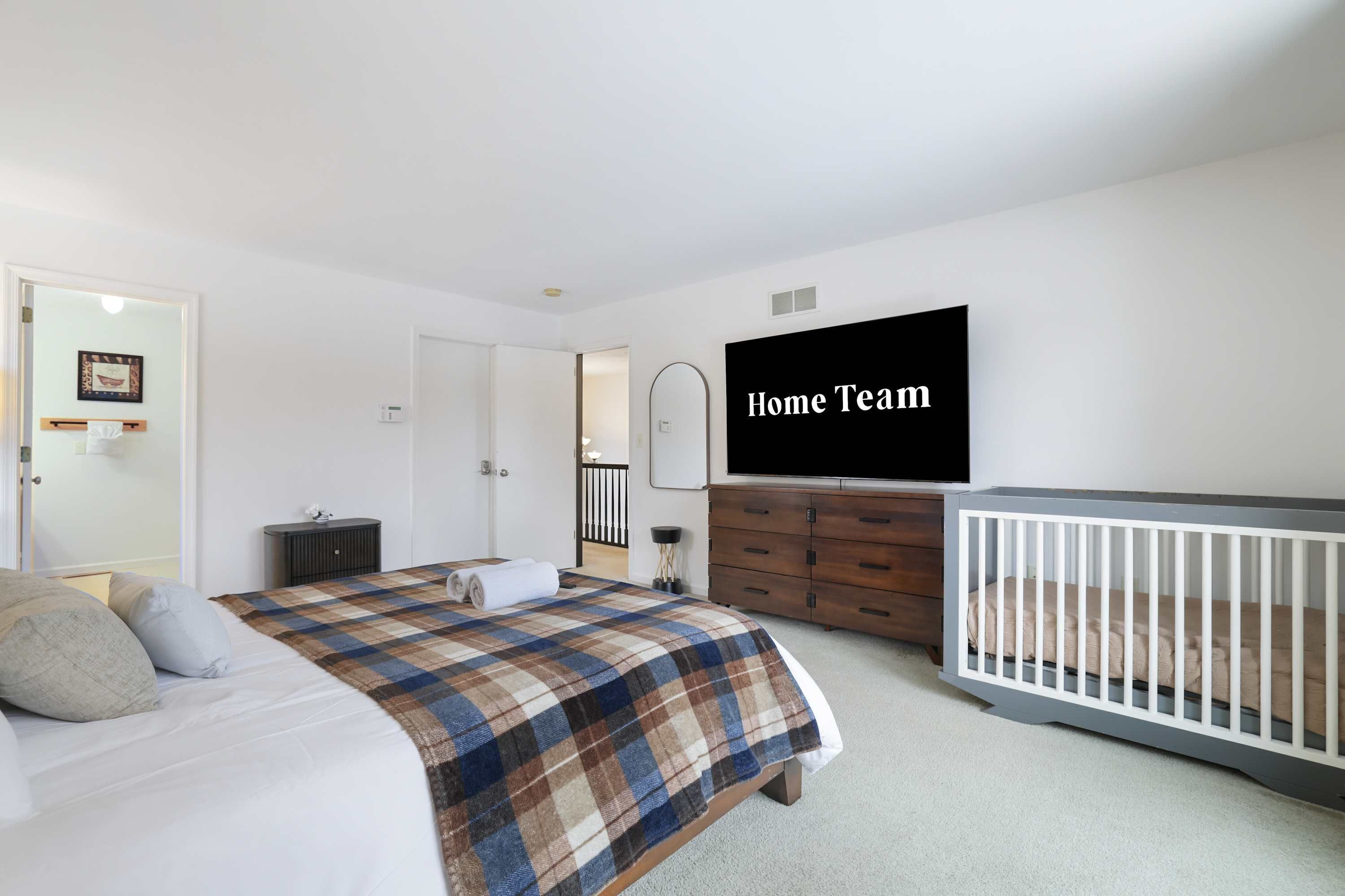 Ein Schlafzimmer mit Bett, Babybett, Kommode, Fernseher und einer Tür zu einem anderen Raum.