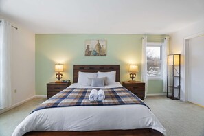 A hotel room with a large bed, two bedside tables with lamps, a window with curtains, and a painting above the bed. - Sleeps 14 Hot Tub Sauna Game Room Fire Pit (Long Pond)