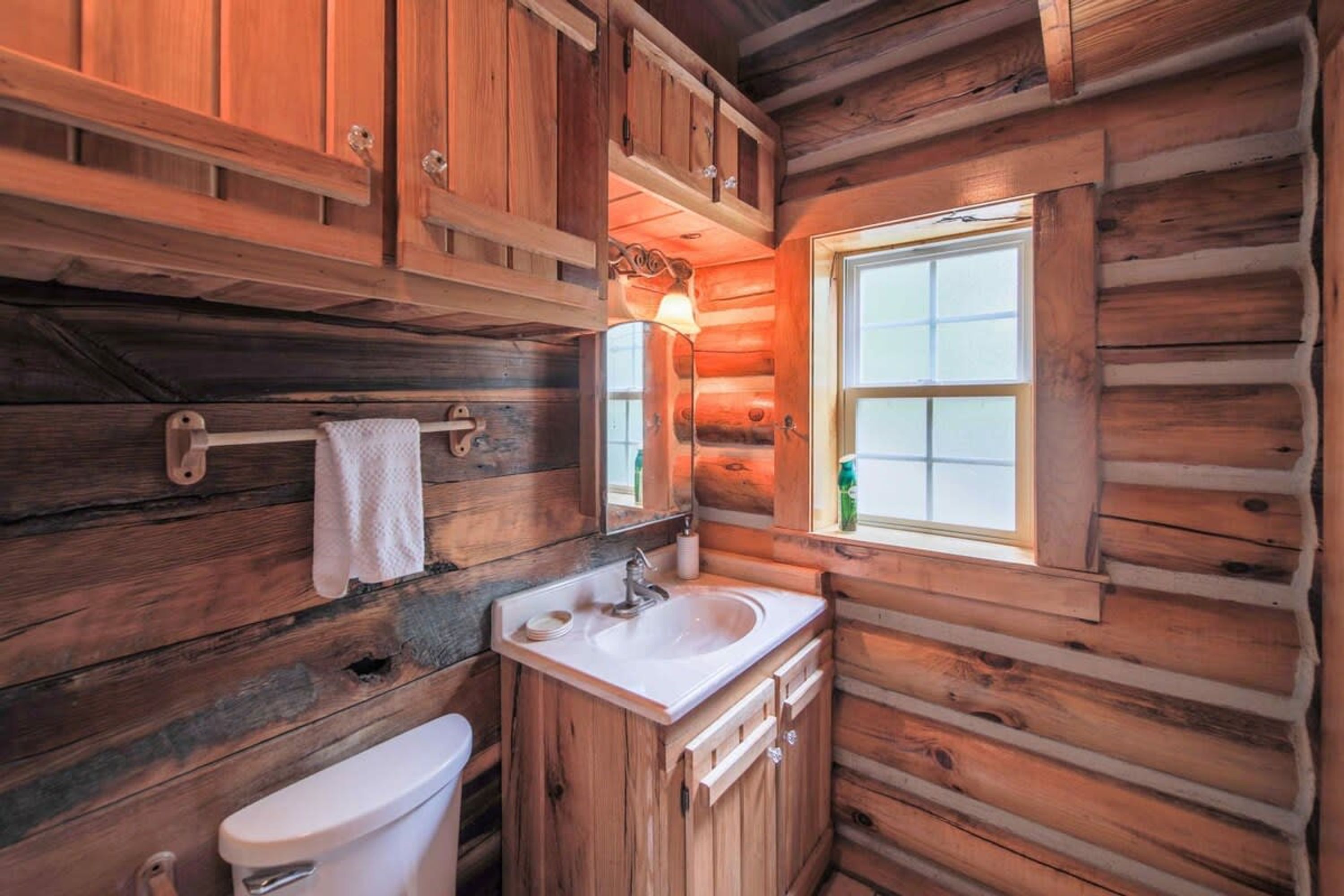A log cabin bathroom with a white sink, a toilet, and wooden cabinets.