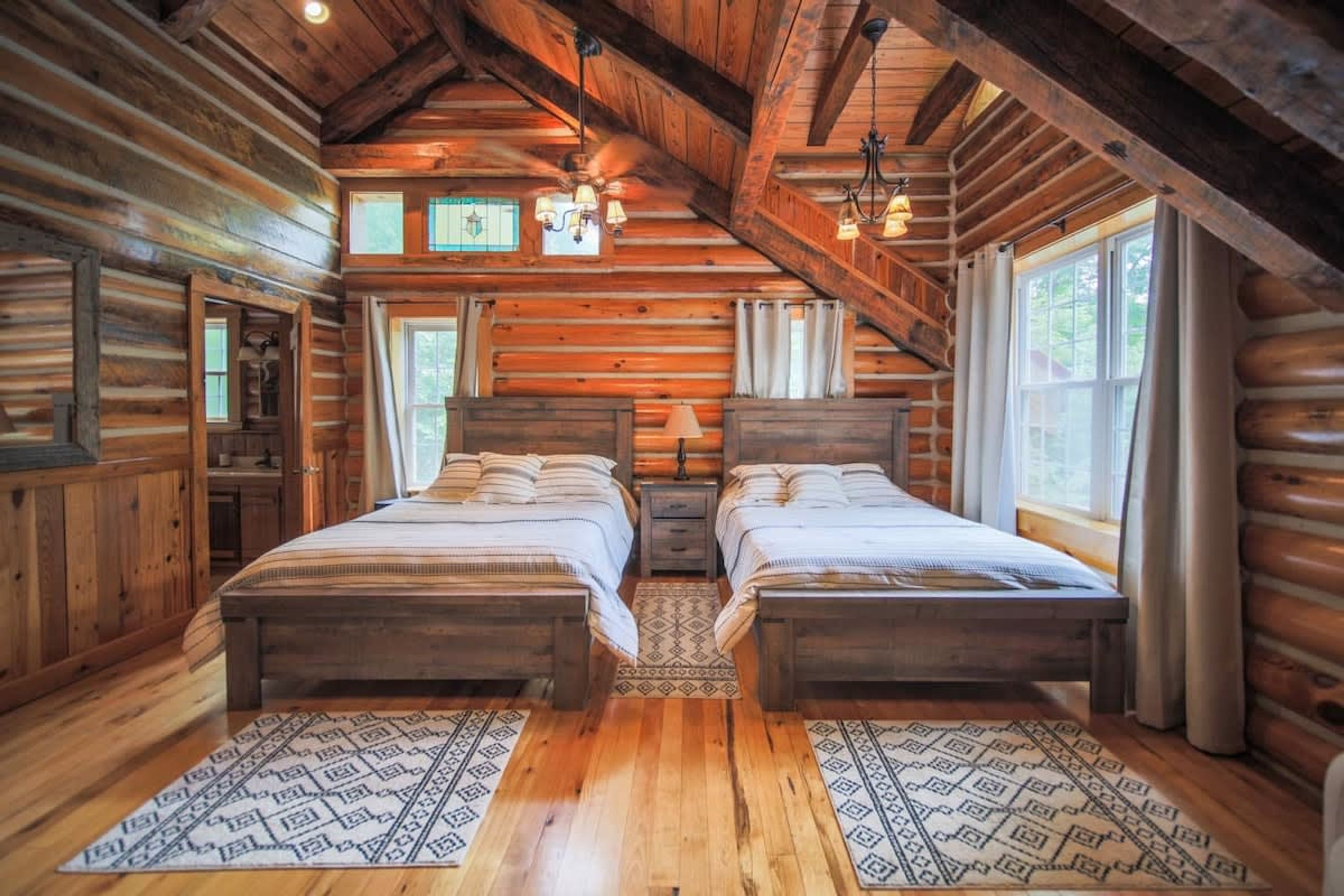 A log cabin bedroom with two beds, wooden floors, and a sloped ceiling.