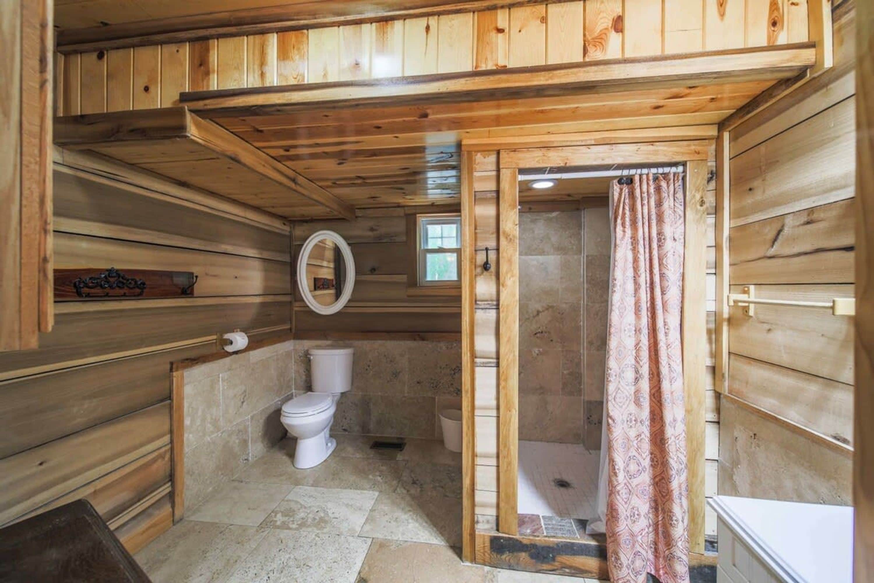 Een kleine houten badkamer met toilet, douche en een klein raam.
