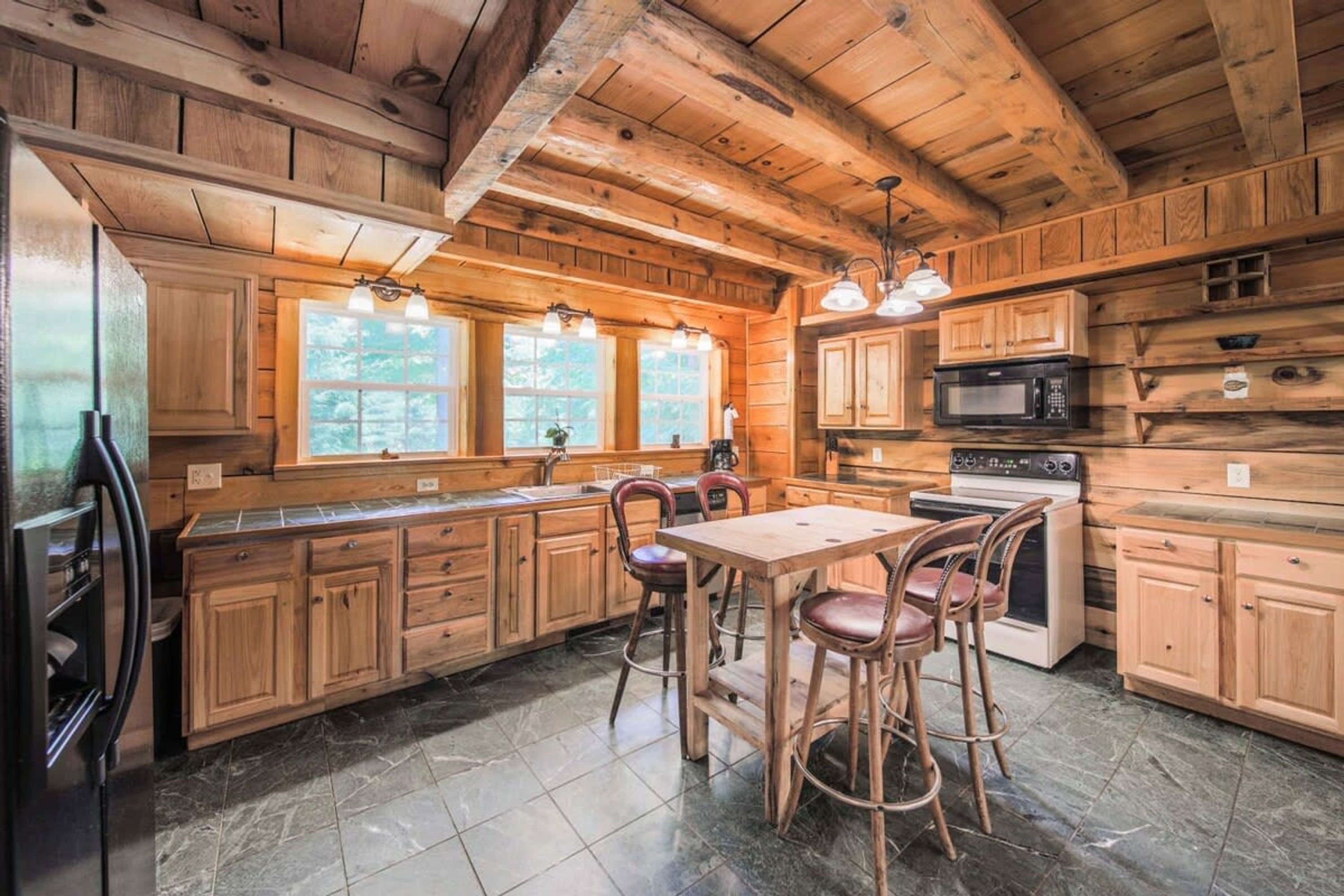A wooden cabin interior with a kitchen area featuring a stove, microwave, and bar stools.