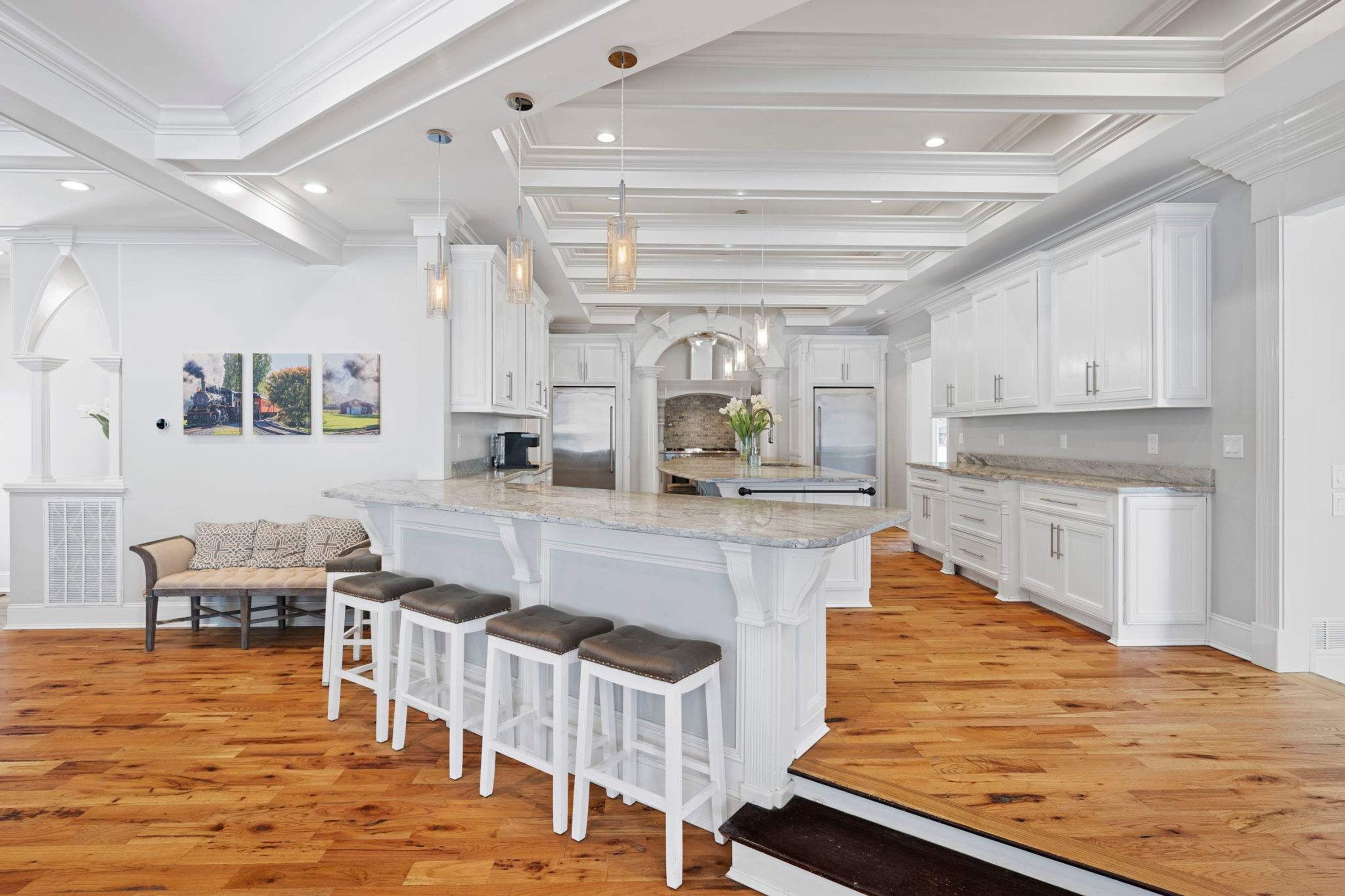 A spacious kitchen with a central island, white cabinetry, and a wooden floor.