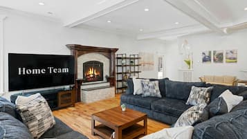 A living room with a fireplace, a sofa set, a coffee table, and a flat-screen TV displaying 'Home Team'.