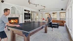 Una mesa de ping pong en una sala de estar con chimenea, televisor y sofá.