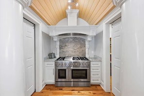 A kitchen with white cabinetry, a stone backsplash, a gas range, and two ovens. - Sleeps 29 Pool Tiki Bar Hot Tub Gym Dogs Welcome (McDonald)