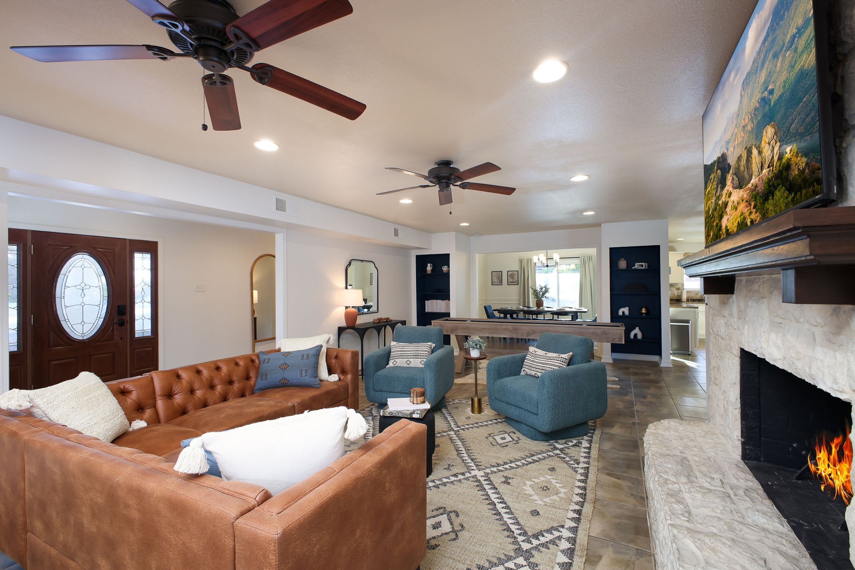 A living room with a fireplace, a ceiling fan, and a kitchen in the background.