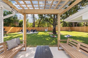 Een overdekt terras met houten banken en een tafel, omringd door een houten hek en bomen.