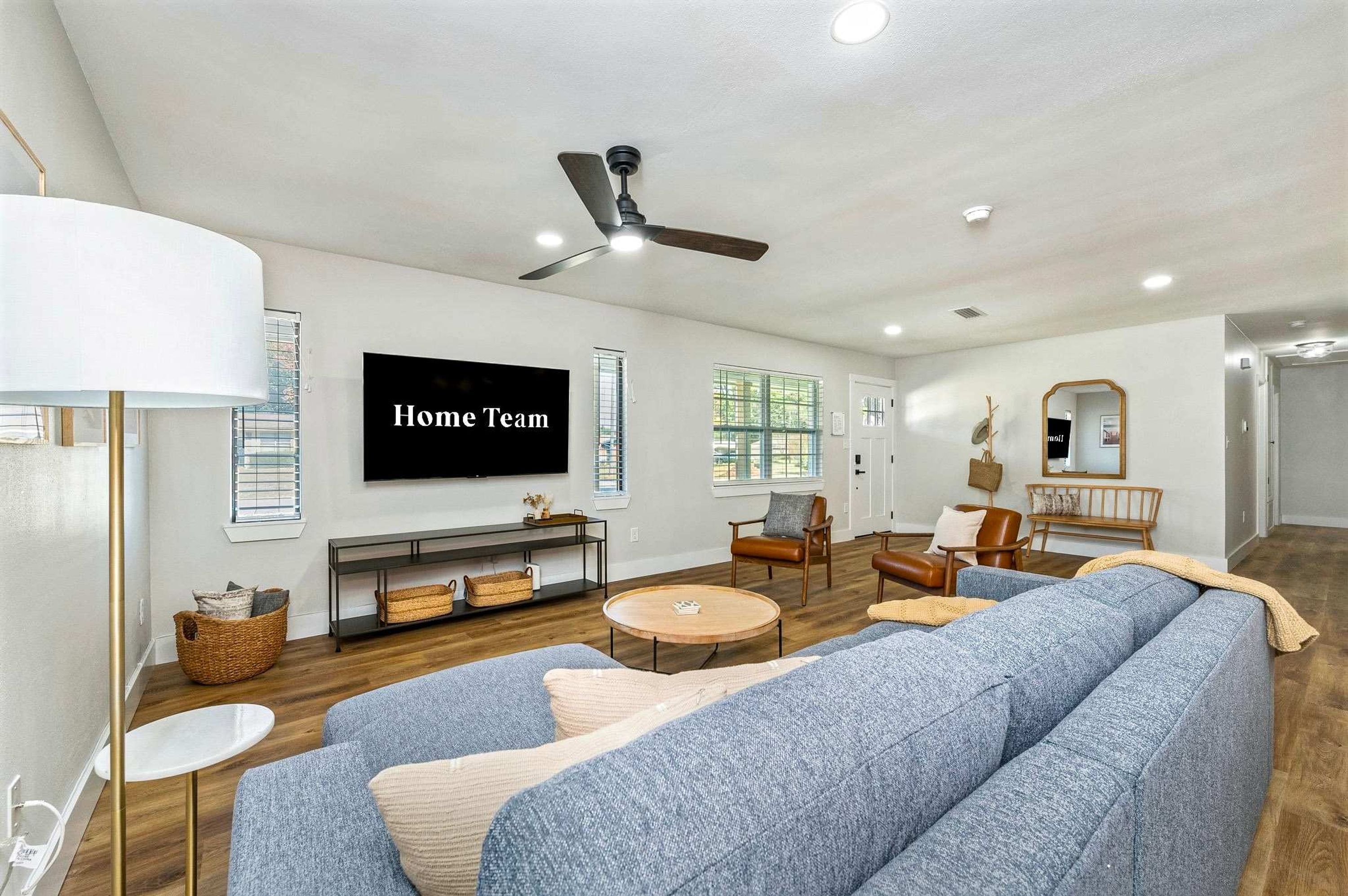A living room with a large flat-screen TV, a ceiling fan, and a fireplace.